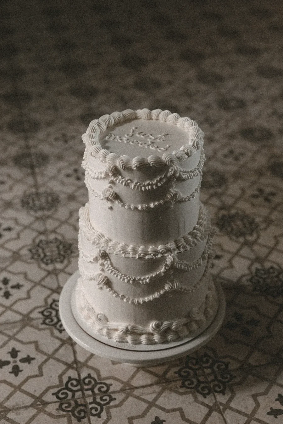 Tarta de boda vintage estilo lambeth en blanco con relieve de manga y mensaje Just Married, sobre suelo de azulejo andalusí, elaborada por Magda Sweet Cakes en Granada.